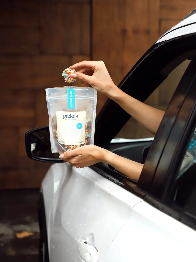 Una mano saca un bite de una bolsa de prekas por la ventana de un coche